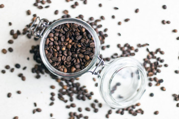 Macro shot of a transparent jar filled with coffee beans in the center of the photo and coffee beans around the jar