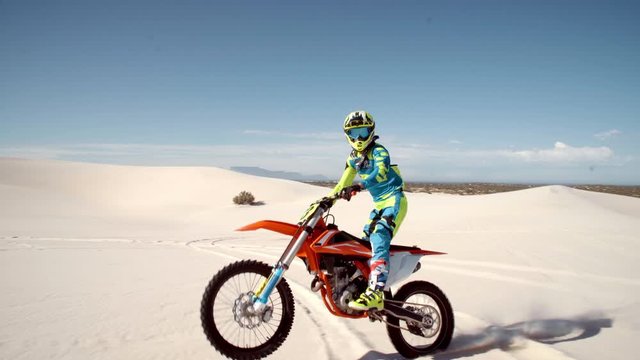 Professional dirt biker riding on sand dunes doing stunts. Motorcyclist riding his bike across desert doing wheelie.

