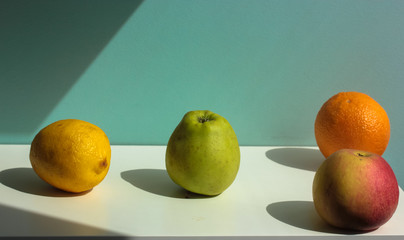 Fruits on the table on a sunny day: apples, lemons, oranges. White background.