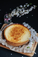 Tasty homemade cheesecake on wooden board and black table with blooming branch.