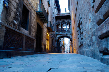 People walking under the Pont del Bisbe at sunrise in the Bari Gotic in Barcelona, Spain