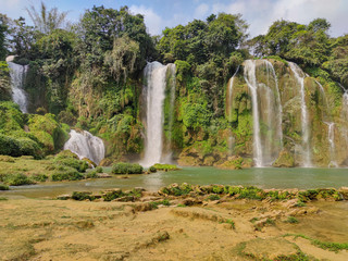 Obraz premium Full of water huge waterfall near the green forest with green trees in mountains