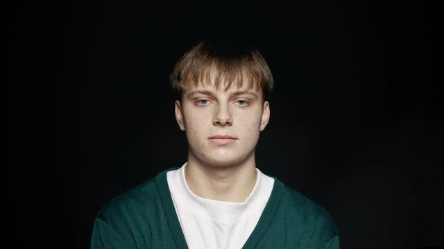 Close up of young man looking at camera against black background. Young man with short brown hair staring at camera.
