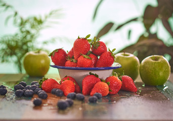 
Fruit still life on a wooden table. There are strawberries, blueberries and apples.