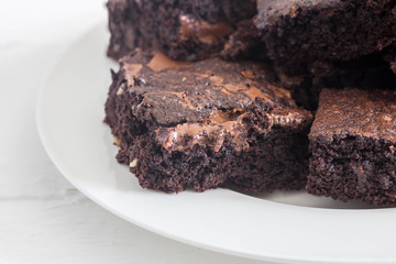 Chocolate brownies with melted chocolate bits stacked in a white plate close up with copy space