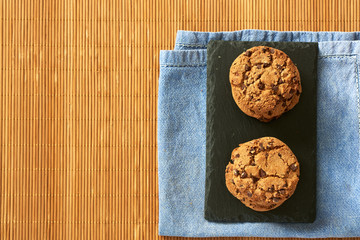 
Chocolate chip cookies on a wooden background with a gray cloth and a black plate.