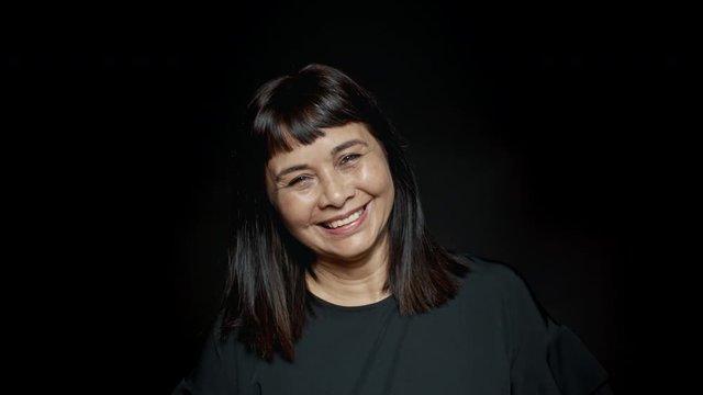 Close up of senior woman laughing on black background. Cheerful middle aged woman looking at camera.
