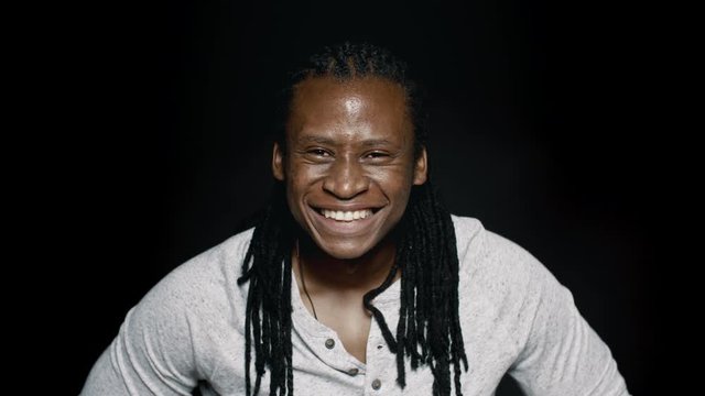 Cheerful african male with dreadlocks on black background. Close up of a laughing young man looking at camera and smiling.
