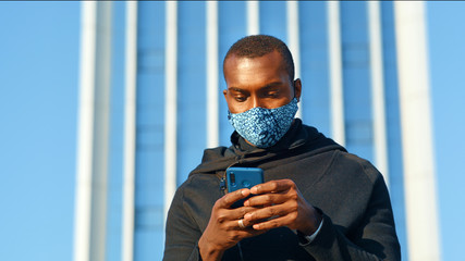 African American man out and about in the city streets during the day, wearing a face mask against...