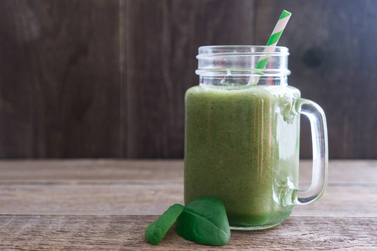 One glass with a pen with a fresh green smoothie of celery, spinach and apple on an old wooden table. Nearby are two green spinach leaves. Place for text