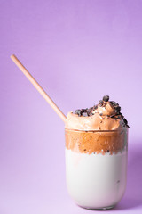Dalgona iced coffee with chocolate chips and straw on purple background. Korean trendy coffee. Vertical picture.