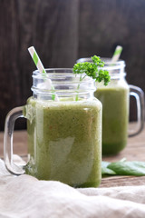 Close-up on two glass cups with handles with a green vegetarian smoothie made from apples, spinach and celery. On an old wooden table and a linen dining napkin nearby.