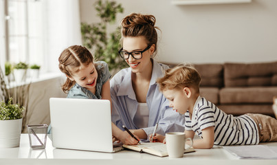 Little children distracting dedicated young woman working on laptop at home.
