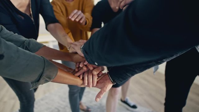 Multi-ethnic businesspeople putting their hands on top of each other and clapping. Business team making a stack of hands showing unity.
