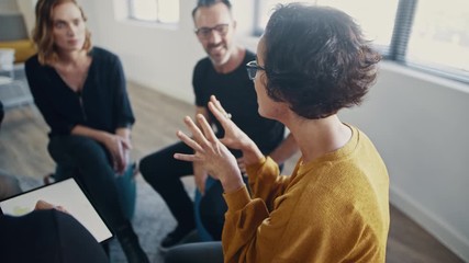 Businesswoman talking during team-building seminar in office. Corporate professionals engaged in personal development training program.
 - Powered by Adobe