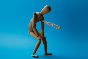  Wooden man figure is in a tired pose with a thermometer /degree meter. Concept of severe old age, fatigue from a long illness and high fever.