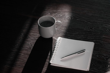 A hot drink in a mug pot on a dark background on the floor - coffee or tea next to a notebook and pen. Flatlay workspace with empty space for text