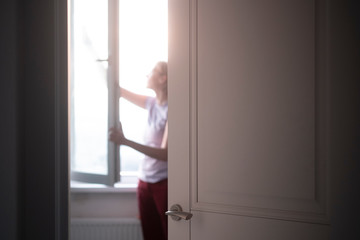 Peeping as a young woman with glasses focused and thoroughly washes a window in an apartment outside the door. Focus in the foreground - doors