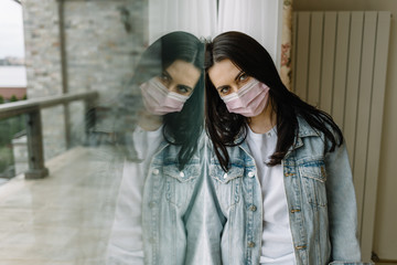 Woman in medical mask near window. Quarantine at home.