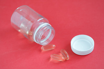 Yellow omega 3 fish oil pills on a red background close-up next to the bottle. Pills and dietary supplement for weight loss and a healthy lifestyle