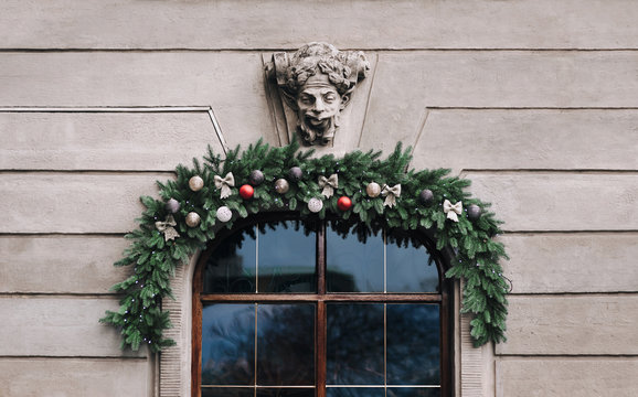 The showcase on the facade is decorated with Christmas wreaths and Christmas decorations. Funny old mascaron with grimace, protruding tongue and open mouth an old house. Lviv, Ukraine.