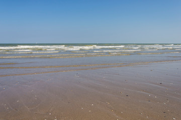 Fototapeta na wymiar Empty beach and oncoming waves of a smooth sea.