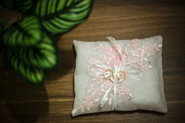A couple of wedding rings on a small  white cushion decorated with pink flowers.