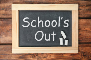 Chalkboard with text SCHOOL'S OUT on wooden background, top view