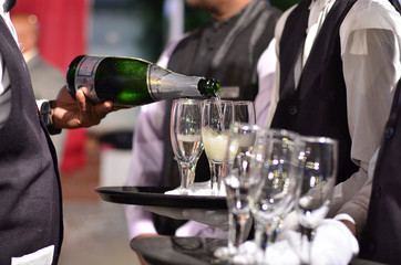 Champagne being poured into empty glasses. Waiters holding  platters with glasses.