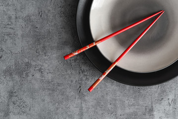 Top view of empty plate and traditional hand painted Japanese red chopsticks. Concrete texture background with copy space. Ceramic plates