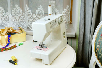 Sewing machine and sewing accessories: scissors, threads, ribbons on the table in the room. Concept - sewing as a hobby