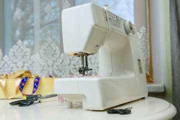 Sewing machine and sewing accessories: scissors, threads, ribbons on the table in the room. Concept - sewing as a hobby