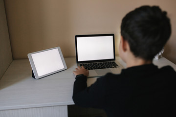 Teenage boy studying on laptop and watching something on tablet. Young boy use two device in same time. Working on laptop and tablet