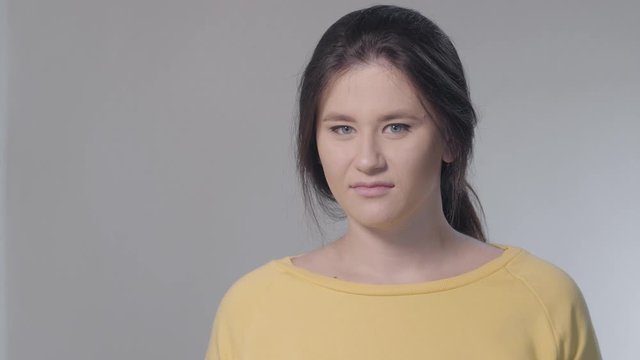 Portrait of young woman with face of contempt. Brunette Caucasian girl with fake smile looking at camera with disdain facial expression. Emotions, feelings, lifestyle, attitude.