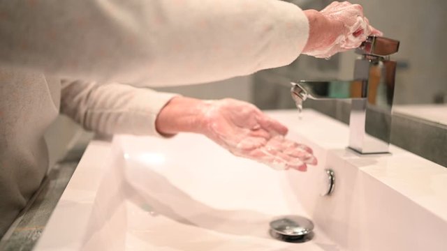 Hand washing lather liquid soap rubbing wrists handwash step senior woman rinsing in water at bathroom faucet sink. Wash hands for COVID-19 spreading prevention. Coronavirus pandemic outbreak.