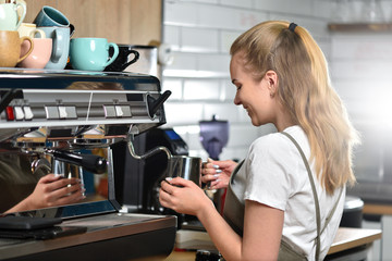 A young barista girl makes coffee on a large professional coffee machine. Small business and student work concept
