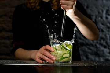 Close-up glass with cocktail which bartender actively mixing using madler.