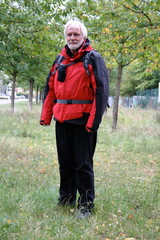 Full length portrait of a white bearded sprightly senior in red black colored active hiking outfit