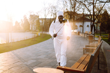 Man wearing protective suit disinfecting public places in the sun with spray chemicals to...