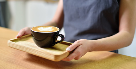 Female barista hands and a large cup of coffee with a pattern on the surface.