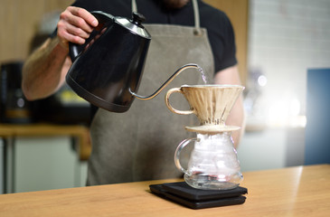 A young barista guy is making coffee with boiling water and a filter. Brewed coffee