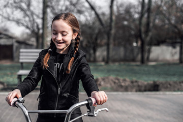 Fototapeta na wymiar Girl on a bike ride. Portrait of a girl with braids in a leather jacket on a bicycle. The girl is joyful and smiling. Sports activity