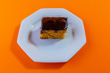 Carrot cake with chocolate topping isolated on orange background. Concept photo.