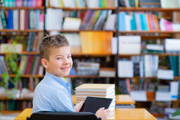 The boy in the library turned around and looked at the camera with a smile, in his hands a tablet computer. Self education concept