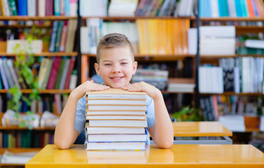 Portrait of cheerful lad sitting in library before book and looking at camera with smile