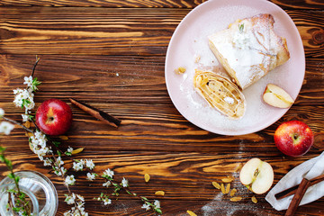 Healthy Home made sweet Apple strudel with raisins and cinnamon on wooden background with blooming fruit branches. Flat Lay. Quarantine kitchen