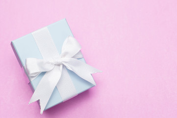Beautiful little blue gift box with silky bow on trendy pastel pink background. Elegant design, main trend of the year 2020. Festive, present and celebration concept.