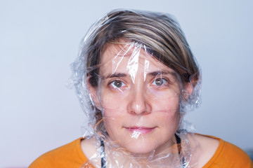 A young woman covered in a plastic wrap looks at the camera with horror. Concept - fruits and leather in the packaging do not breathe. Domestic violence
