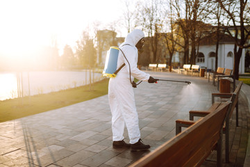 Man wearing protective suit disinfecting public places in the sun with spray chemicals to...
