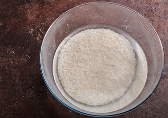 white basmati rice in water in a glass bowl on a brown background